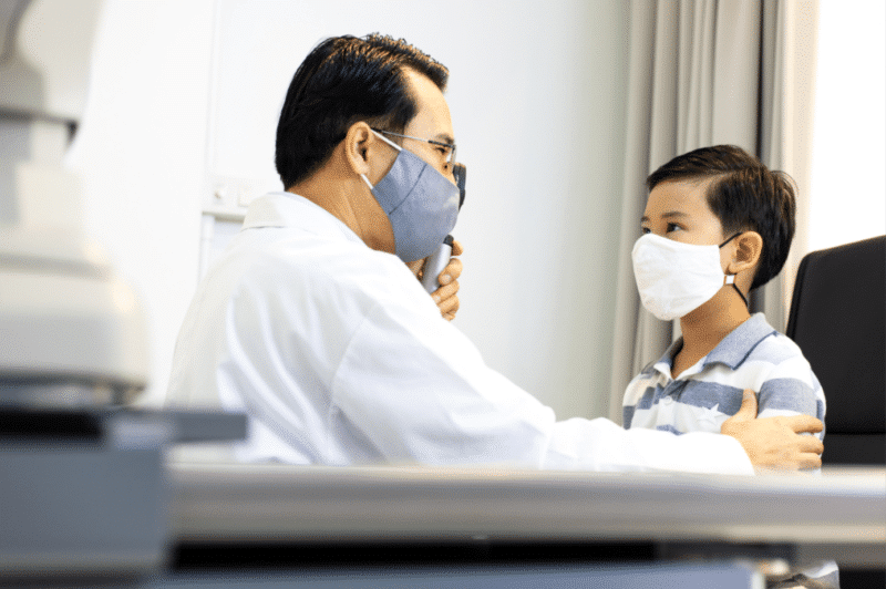Optometrist wearing a mask examining the eyes of a young boy wearing a mask